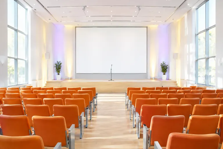 Auditorium lumineux aux sièges orange avec une scène, un micro et un écran vierge