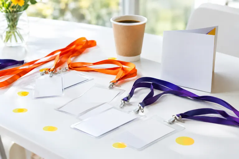 Badges d’intervenant vierges sur cordons orange et violets posés sur une table blanche